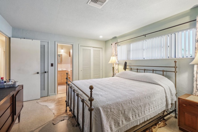 bedroom featuring ensuite bathroom, a textured ceiling, and light carpet