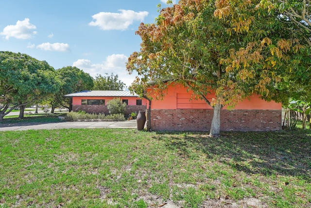 exterior space featuring a standing seam roof, metal roof, brick siding, and a lawn