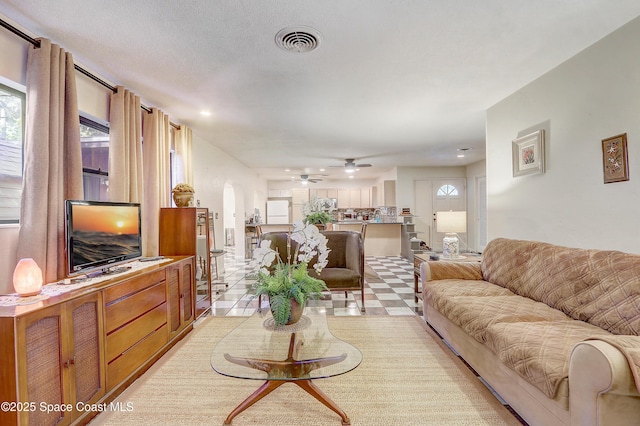 living area featuring ceiling fan, visible vents, arched walkways, and a wealth of natural light