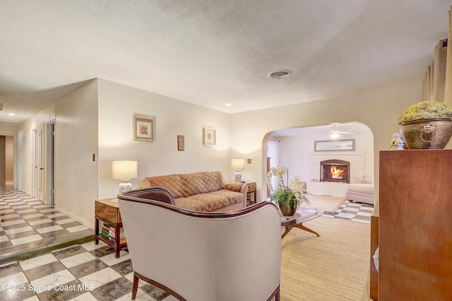 living area featuring a textured ceiling, arched walkways, visible vents, a lit fireplace, and light floors