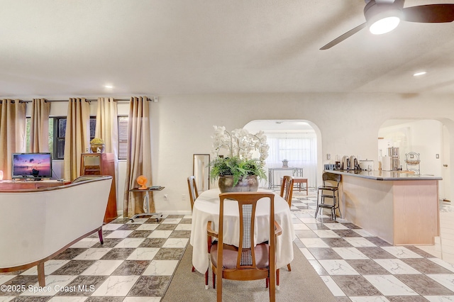 dining area with arched walkways, ceiling fan, and light floors