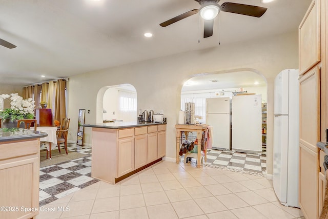 kitchen with arched walkways, dark countertops, freestanding refrigerator, light brown cabinetry, and light floors