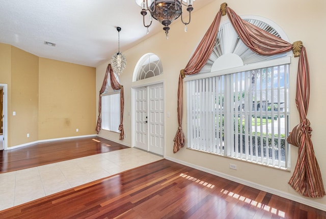 entrance foyer with hardwood / wood-style floors, vaulted ceiling, and an inviting chandelier