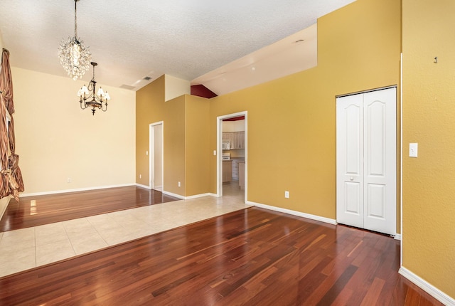 unfurnished room with hardwood / wood-style flooring, a notable chandelier, a textured ceiling, and high vaulted ceiling