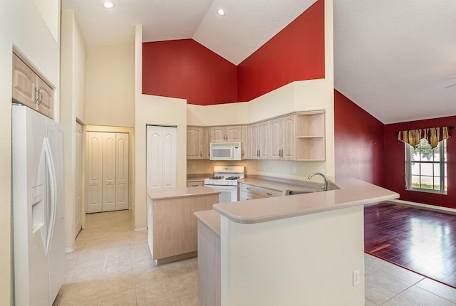 kitchen with high vaulted ceiling, kitchen peninsula, white appliances, light brown cabinetry, and a kitchen island