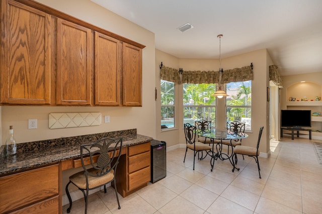 kitchen featuring hanging light fixtures, wine cooler, dark stone countertops, built in desk, and light tile patterned flooring