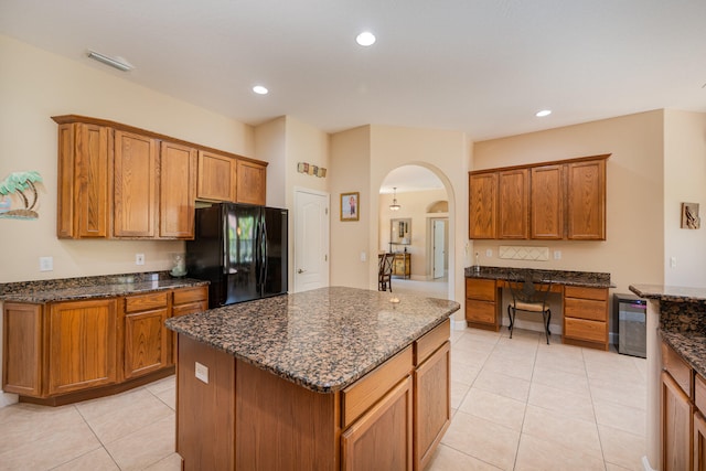 kitchen with dark stone countertops, black fridge, a center island, and light tile patterned floors