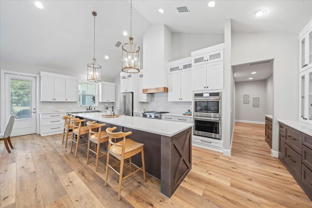 kitchen featuring light hardwood / wood-style floors, tasteful backsplash, stainless steel appliances, a center island with sink, and white cabinets