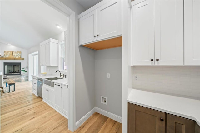 kitchen featuring vaulted ceiling, light hardwood / wood-style flooring, tasteful backsplash, white cabinetry, and sink