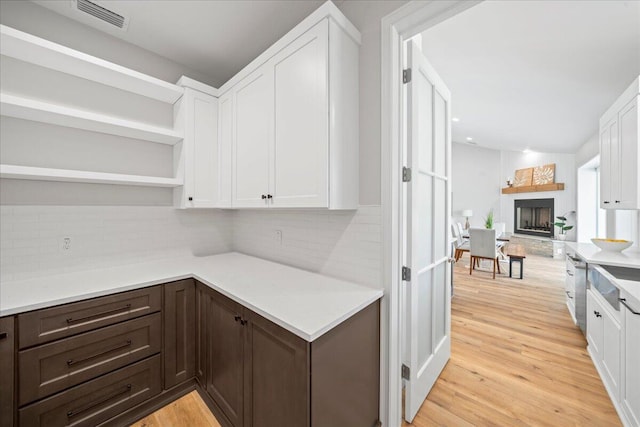 kitchen featuring dark brown cabinetry, light hardwood / wood-style flooring, white cabinets, and backsplash