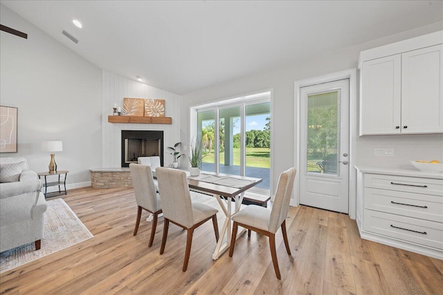 dining space with a fireplace, lofted ceiling, and light wood-type flooring