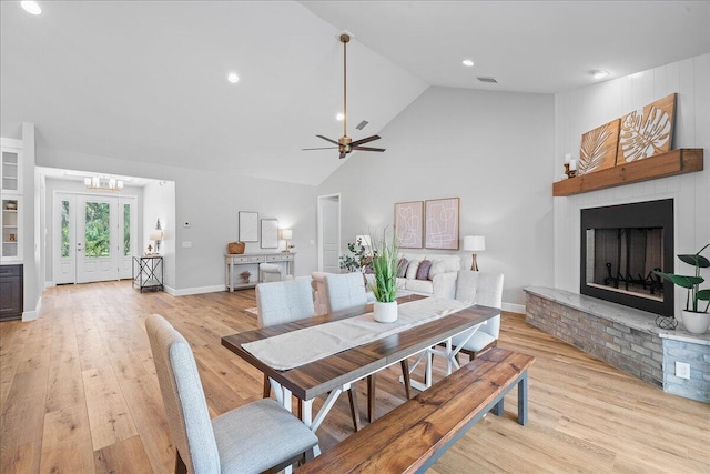 dining area featuring ceiling fan, light hardwood / wood-style flooring, french doors, a fireplace, and high vaulted ceiling