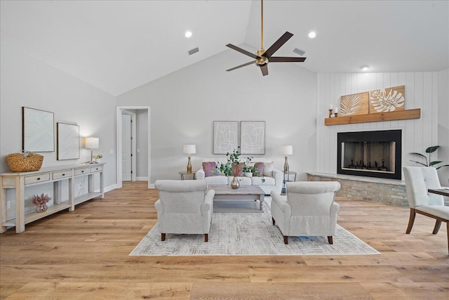 living room featuring high vaulted ceiling, ceiling fan, a large fireplace, and light hardwood / wood-style flooring