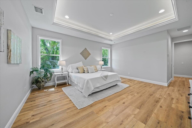 bedroom with a tray ceiling, light wood-type flooring, and crown molding