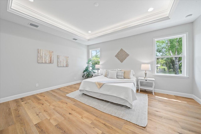 bedroom with light hardwood / wood-style floors, a tray ceiling, and crown molding