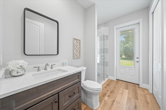 bathroom with toilet, vanity, hardwood / wood-style flooring, and a shower with door