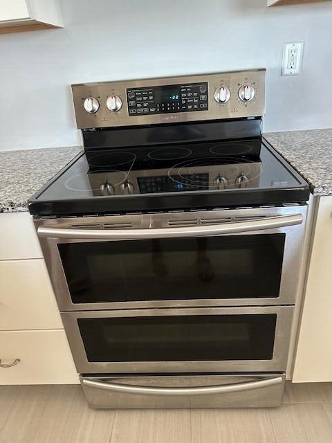 details featuring white cabinets, double oven range, and light stone counters