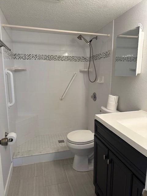 bathroom featuring vanity, a textured ceiling, tiled shower, and toilet