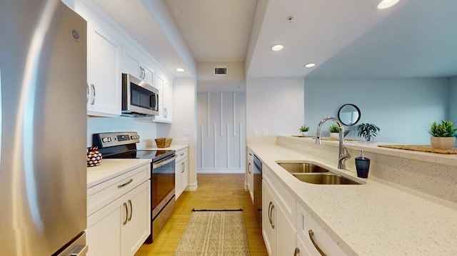 kitchen featuring white cabinets, stainless steel appliances, light stone countertops, light wood-type flooring, and sink