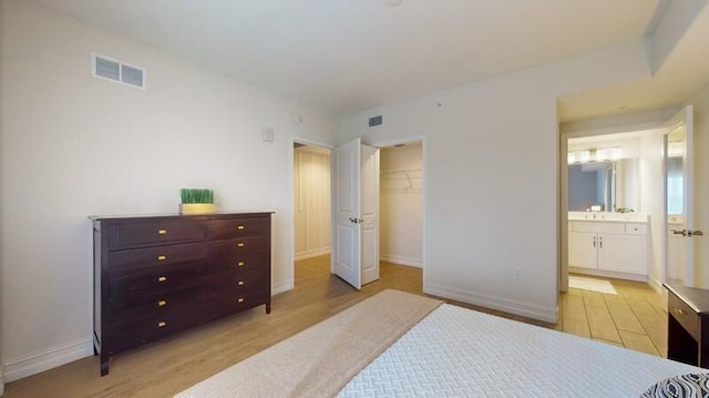 bedroom featuring a walk in closet, a closet, ensuite bathroom, and light wood-type flooring