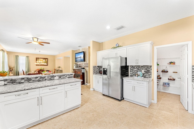 kitchen with white cabinets, stainless steel refrigerator with ice dispenser, ceiling fan, decorative backsplash, and light stone counters