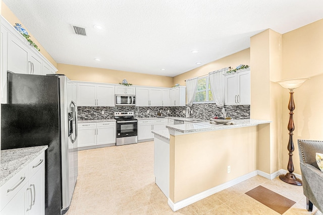 kitchen with white cabinets, appliances with stainless steel finishes, kitchen peninsula, and light stone countertops