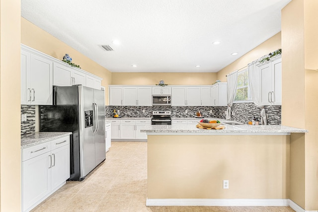 kitchen with kitchen peninsula, stainless steel appliances, white cabinetry, and light stone countertops