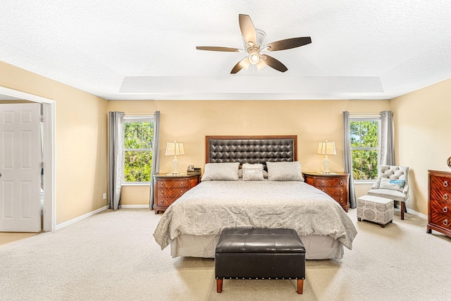 carpeted bedroom featuring a raised ceiling, multiple windows, and ceiling fan