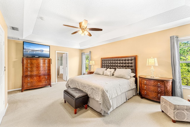 carpeted bedroom featuring a tray ceiling, ensuite bath, ceiling fan, and a textured ceiling