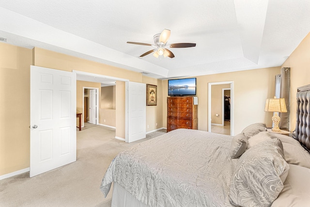 bedroom featuring a raised ceiling, ceiling fan, light carpet, and a textured ceiling