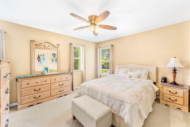 bedroom with ceiling fan, light colored carpet, and a textured ceiling