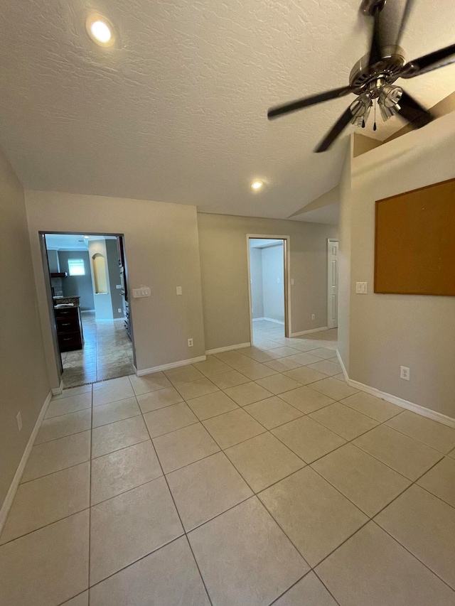 spare room with lofted ceiling, ceiling fan, light tile patterned flooring, and a textured ceiling