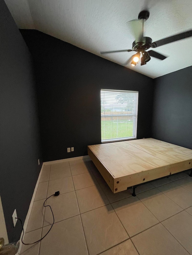 unfurnished bedroom featuring ceiling fan, a textured ceiling, light tile patterned floors, and lofted ceiling