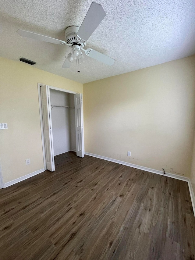 unfurnished bedroom with ceiling fan, a textured ceiling, dark hardwood / wood-style flooring, and a closet