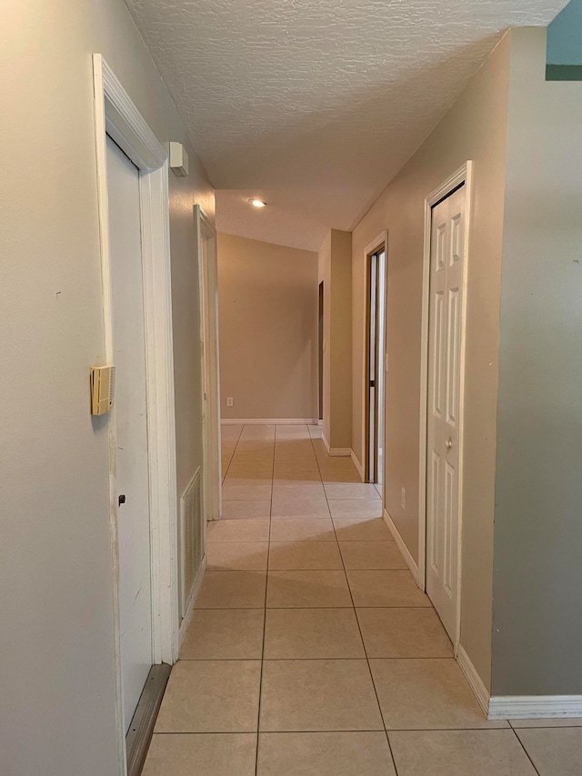 hall with a textured ceiling and light tile patterned floors