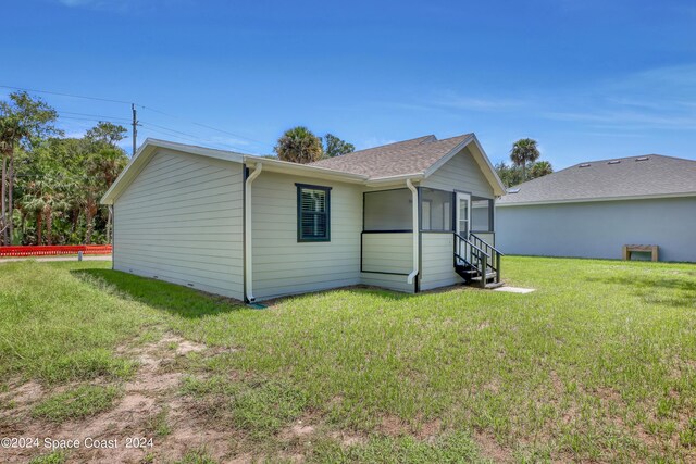 702 S Myrtle Ave, New Smyrna Beach, FL 32168 - rear view of house featuring a sunroom, a shingled roof, and a yard