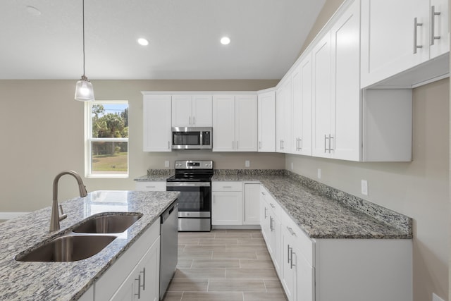 kitchen with light stone counters, stainless steel appliances, sink, white cabinetry, and hanging light fixtures