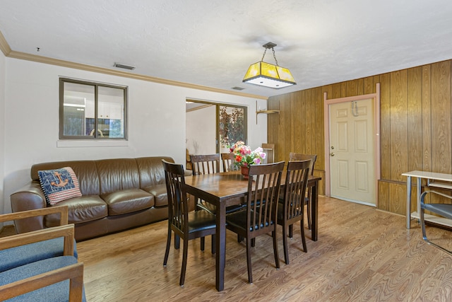 dining room featuring wood walls, ornamental molding, and light hardwood / wood-style floors