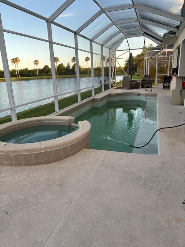 pool at dusk featuring a lanai, a patio area, an in ground hot tub, and a water view