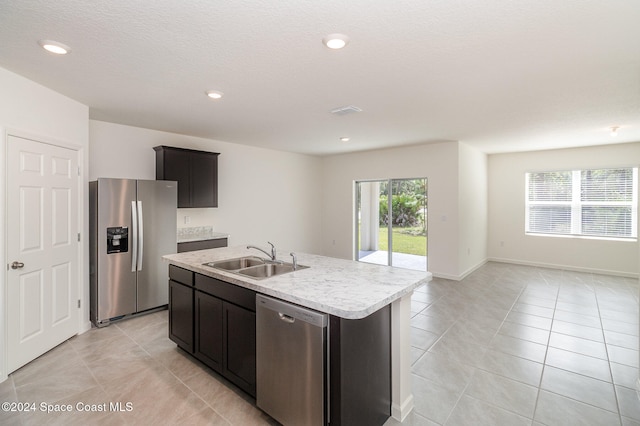 kitchen with light tile patterned flooring, sink, stainless steel appliances, and a kitchen island with sink