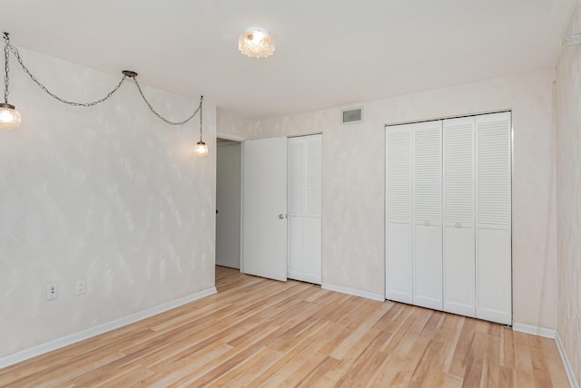 unfurnished bedroom featuring multiple closets and light hardwood / wood-style flooring