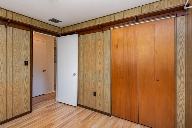 unfurnished bedroom featuring light wood-type flooring, a closet, and wood walls