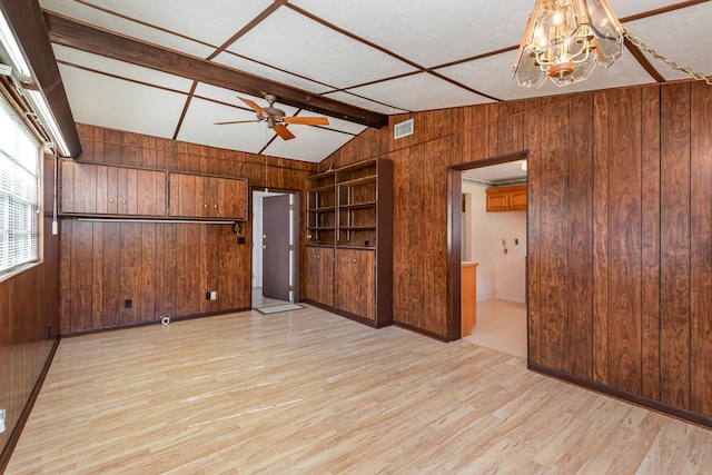 empty room featuring vaulted ceiling, wood walls, light hardwood / wood-style floors, and ceiling fan with notable chandelier