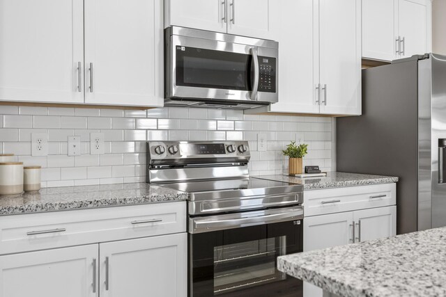 kitchen featuring stainless steel appliances, white cabinetry, light stone countertops, and backsplash