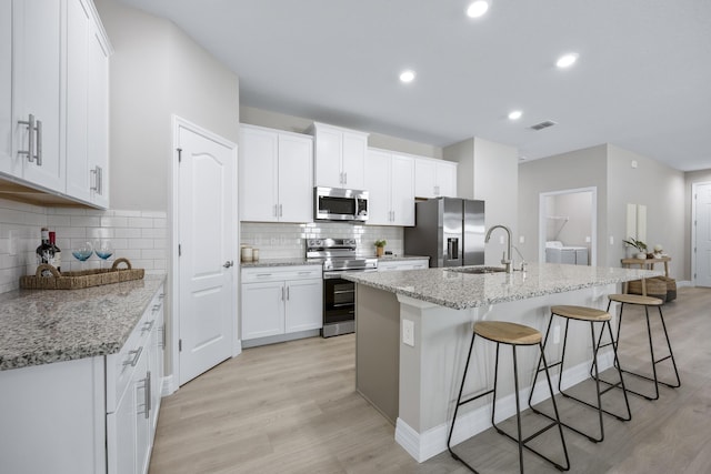 kitchen featuring washing machine and clothes dryer, white cabinetry, stainless steel appliances, light stone counters, and a kitchen island with sink