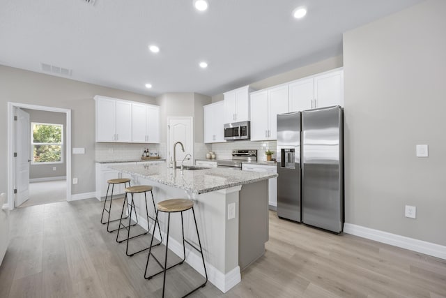 kitchen with appliances with stainless steel finishes, an island with sink, white cabinets, a kitchen breakfast bar, and light stone countertops