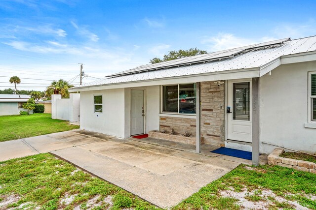 1557 Hillcrest Dr, Melbourne, FL 32935 - doorway to property with stucco siding, stone siding, solar panels, a yard, and metal roof