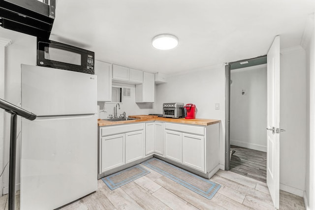 kitchen featuring sink, white refrigerator, light hardwood / wood-style flooring, white cabinets, and butcher block countertops