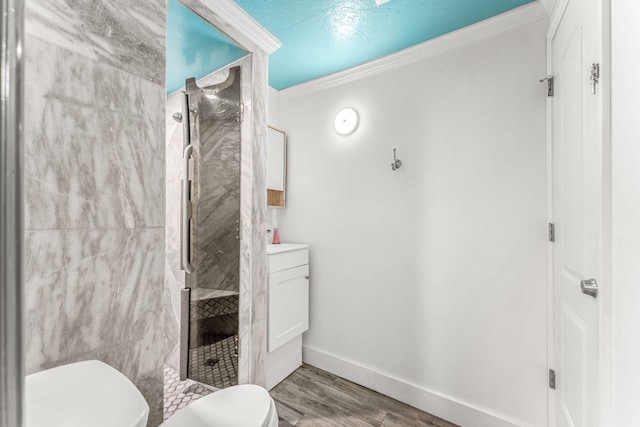 bathroom featuring vanity, toilet, ornamental molding, a tile shower, and wood-type flooring