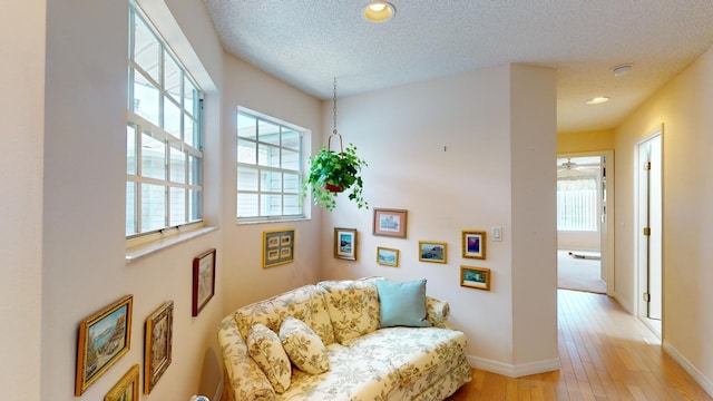 living area with ceiling fan, light wood-type flooring, and a textured ceiling